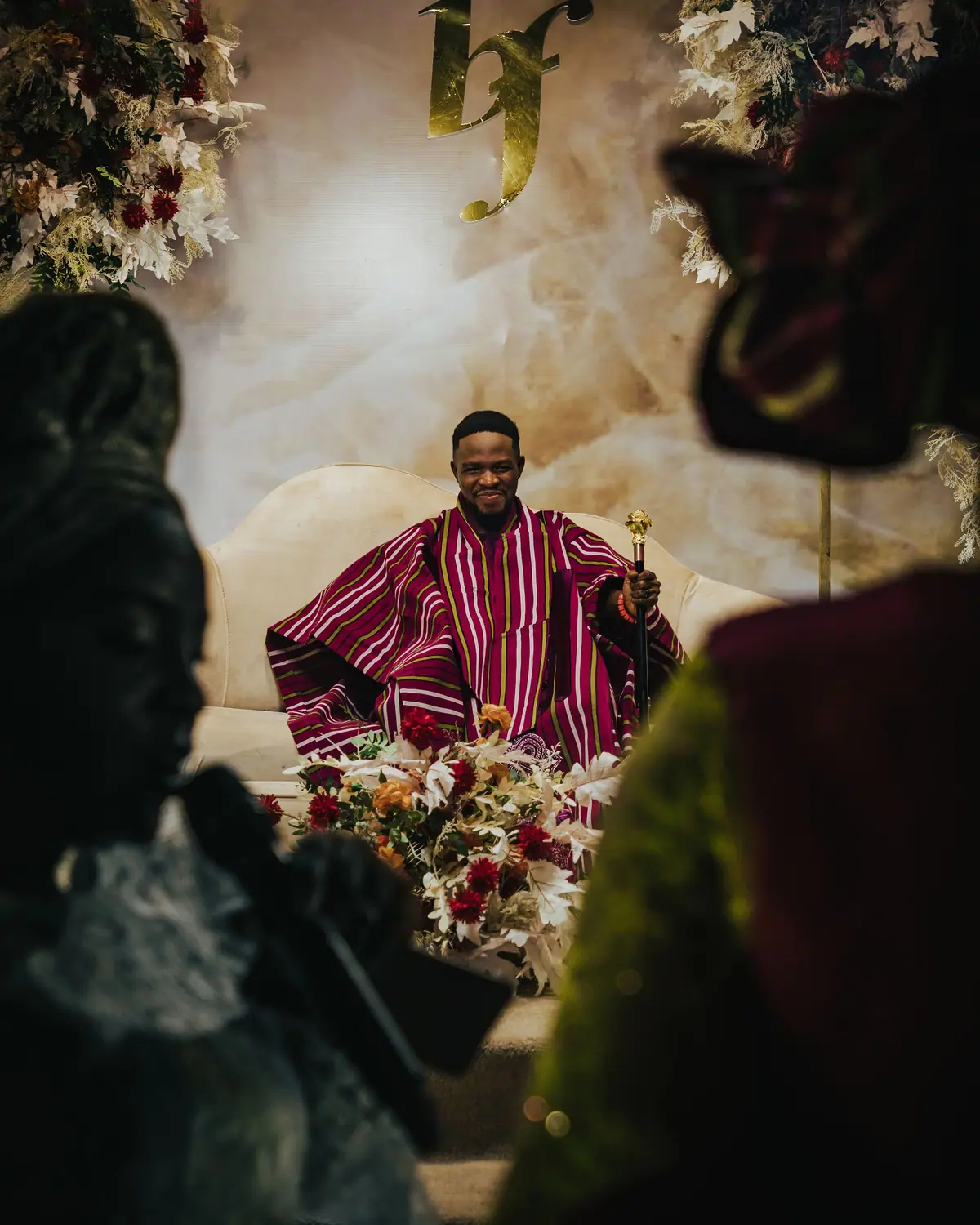A man in a magenta traditional robe seated on a decorated ceremony stage.