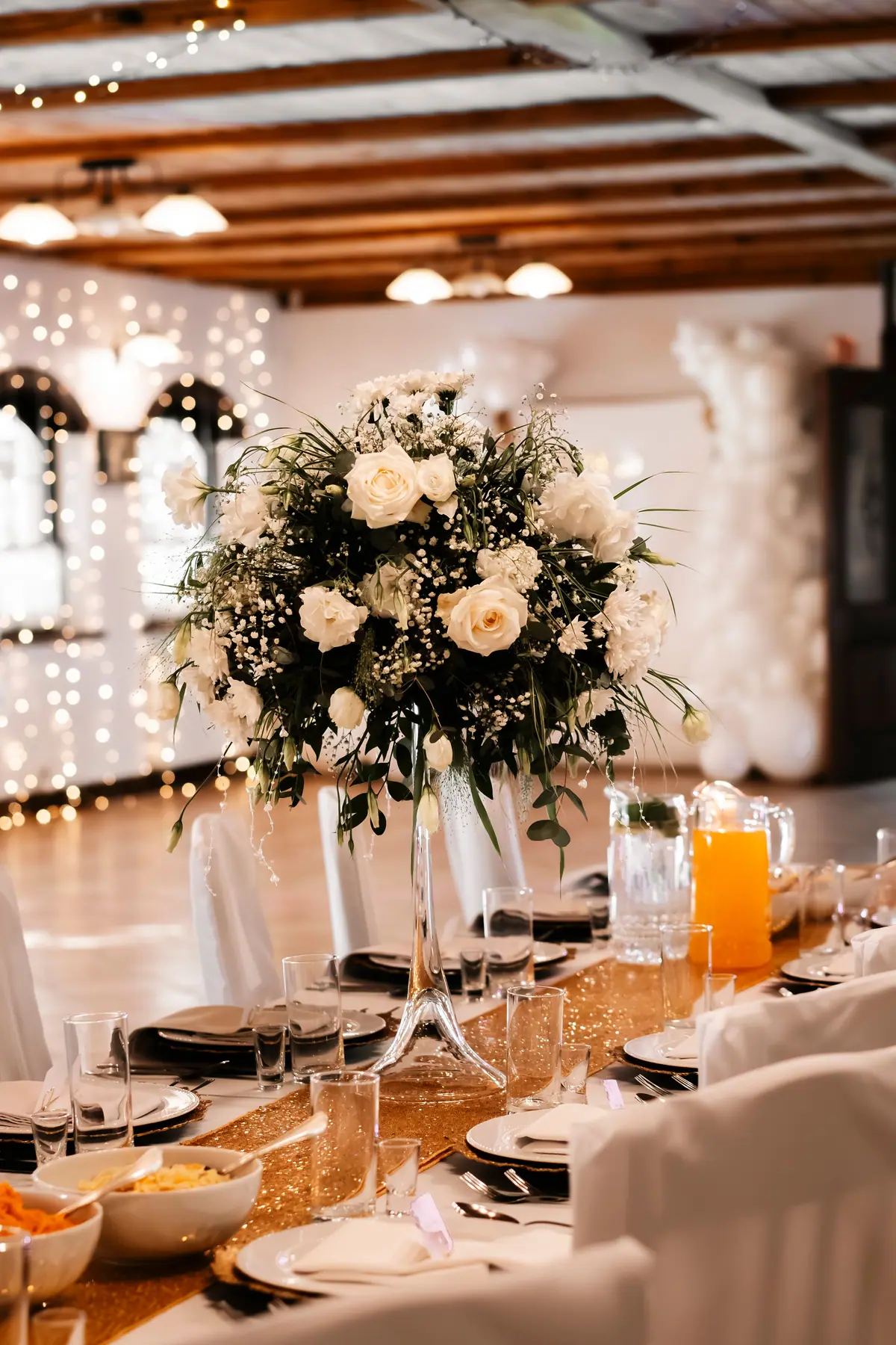 A round table with a tall floral centrepiece, candles and place settings.