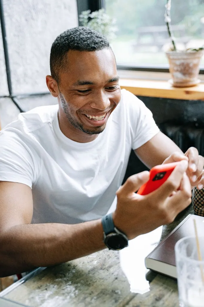 A customer smiling while using a smartphone at a cafe table.