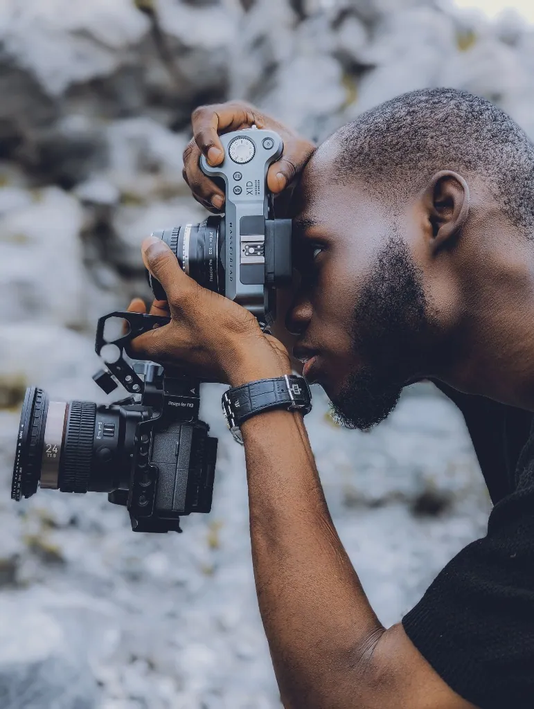 A photographer looking through a camera viewfinder while working outdoors.