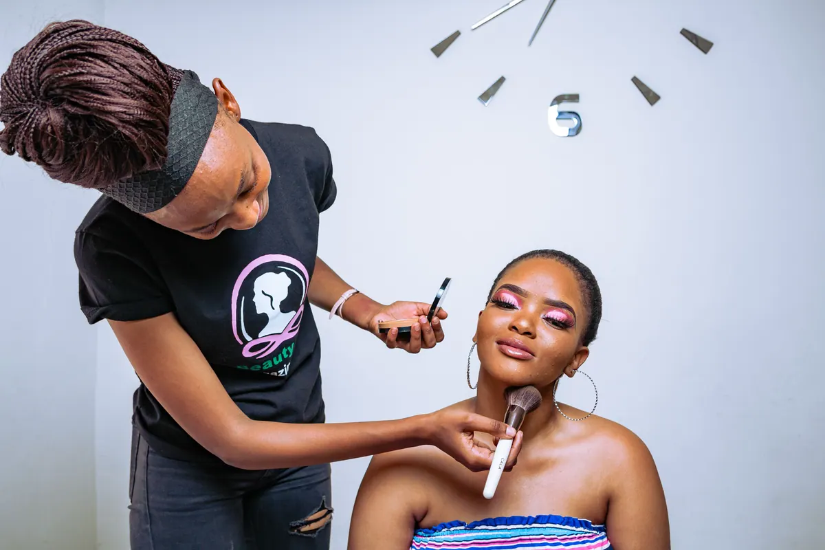 A makeup artist applying foundation to a client with a brush.