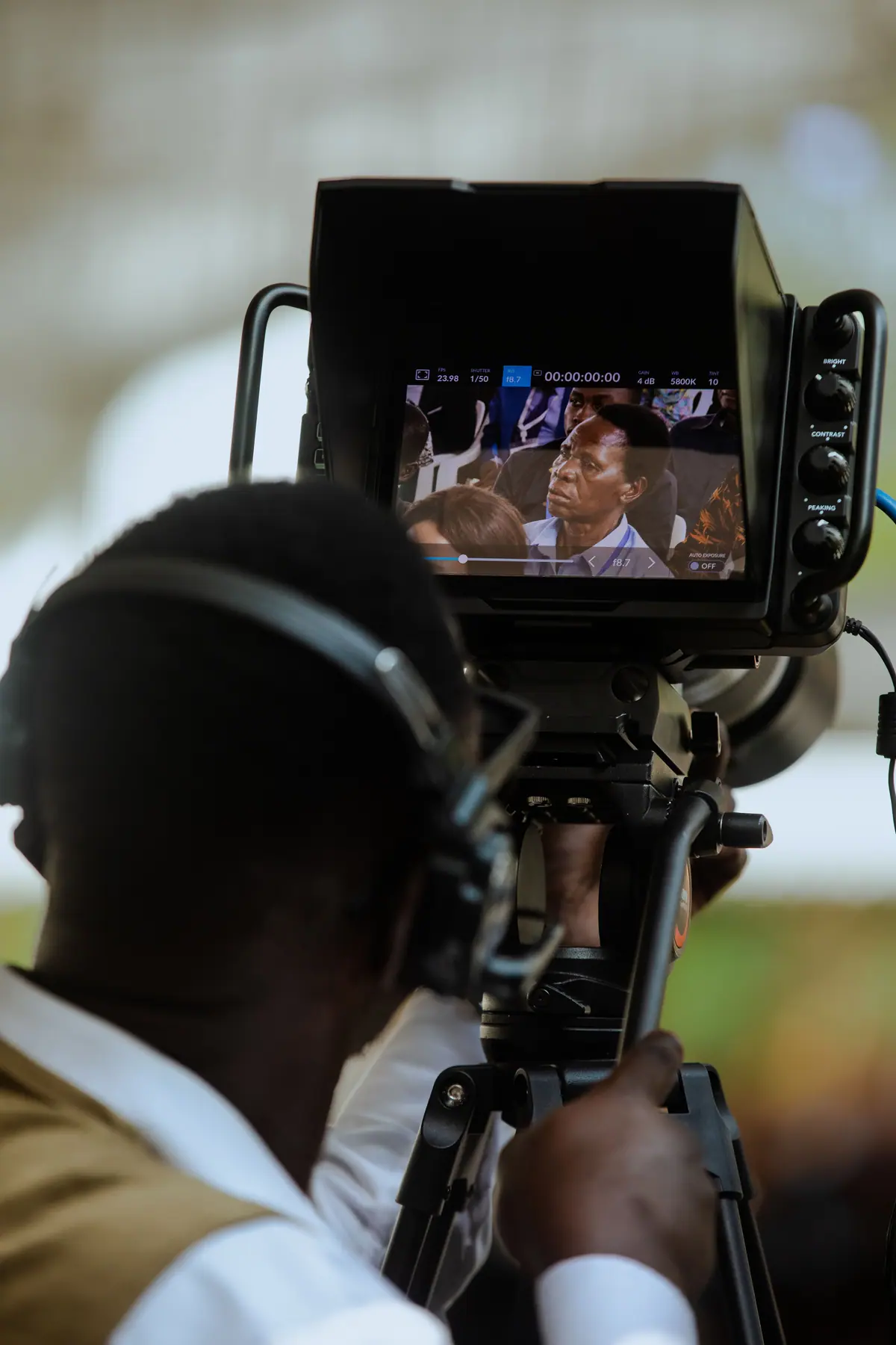 A videographer wearing headphones operating a camera monitor at an event.