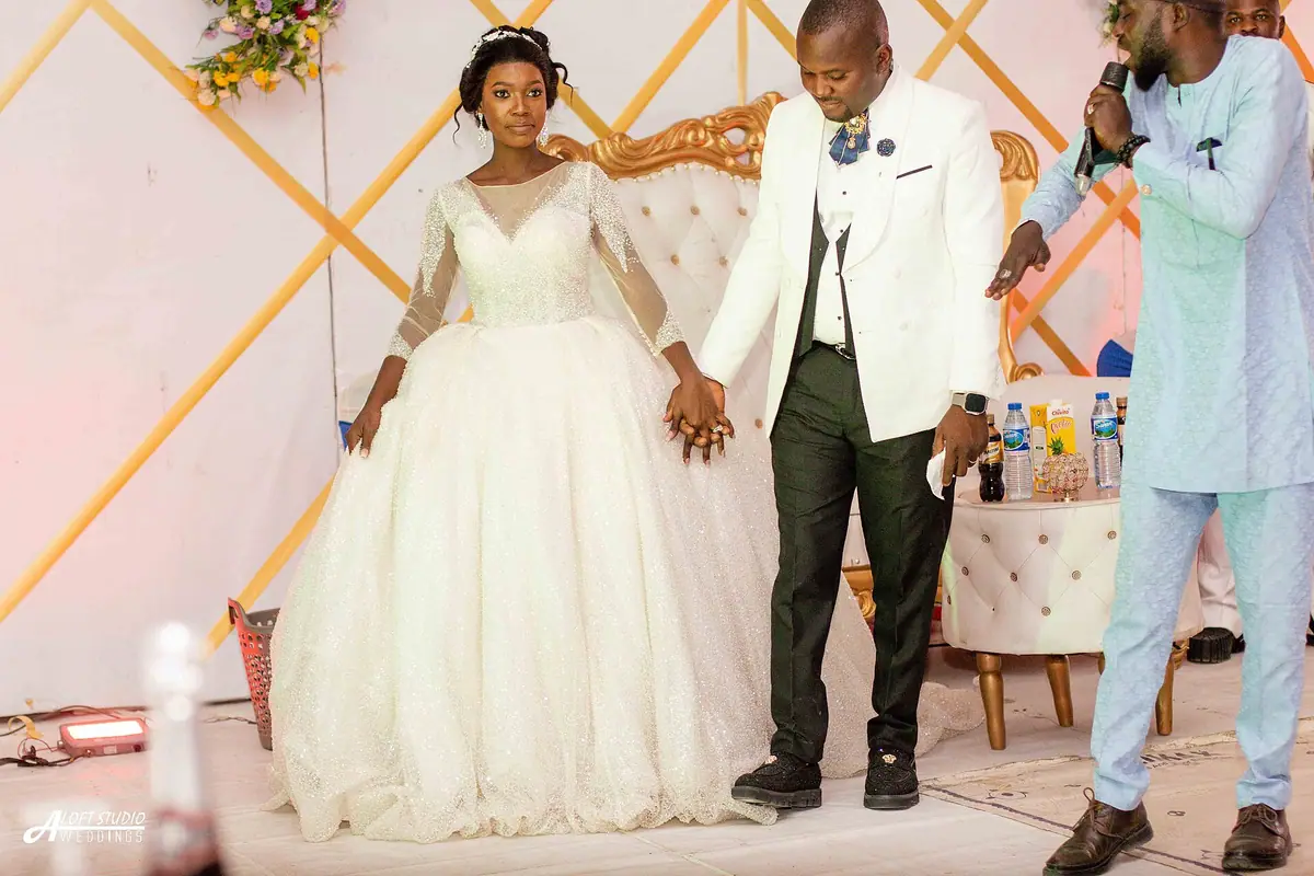 A bride in a white ball gown holding hands with a groom in a white jacket.